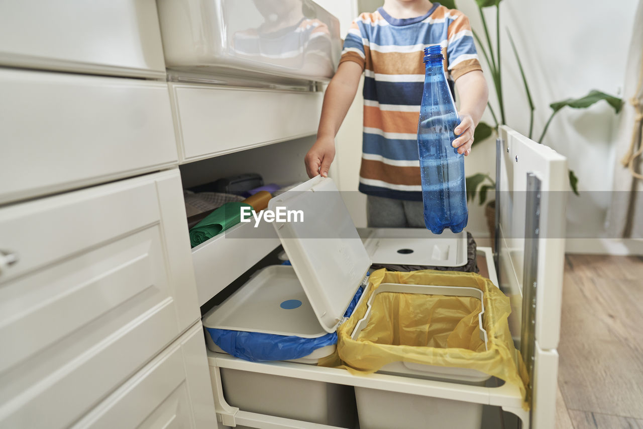 Boy throwing plastic bottle in garbage bin at home