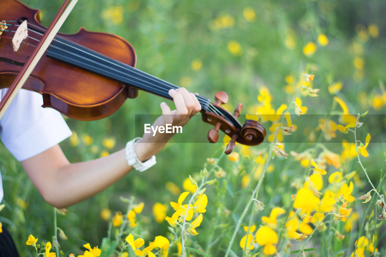 Woman playing violin by yellow flowers on field