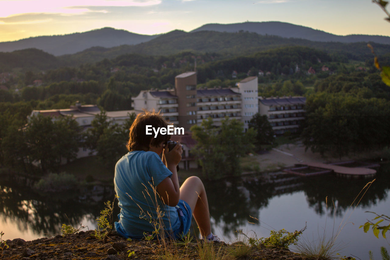 Rear view of boy photographing while sitting on mountain