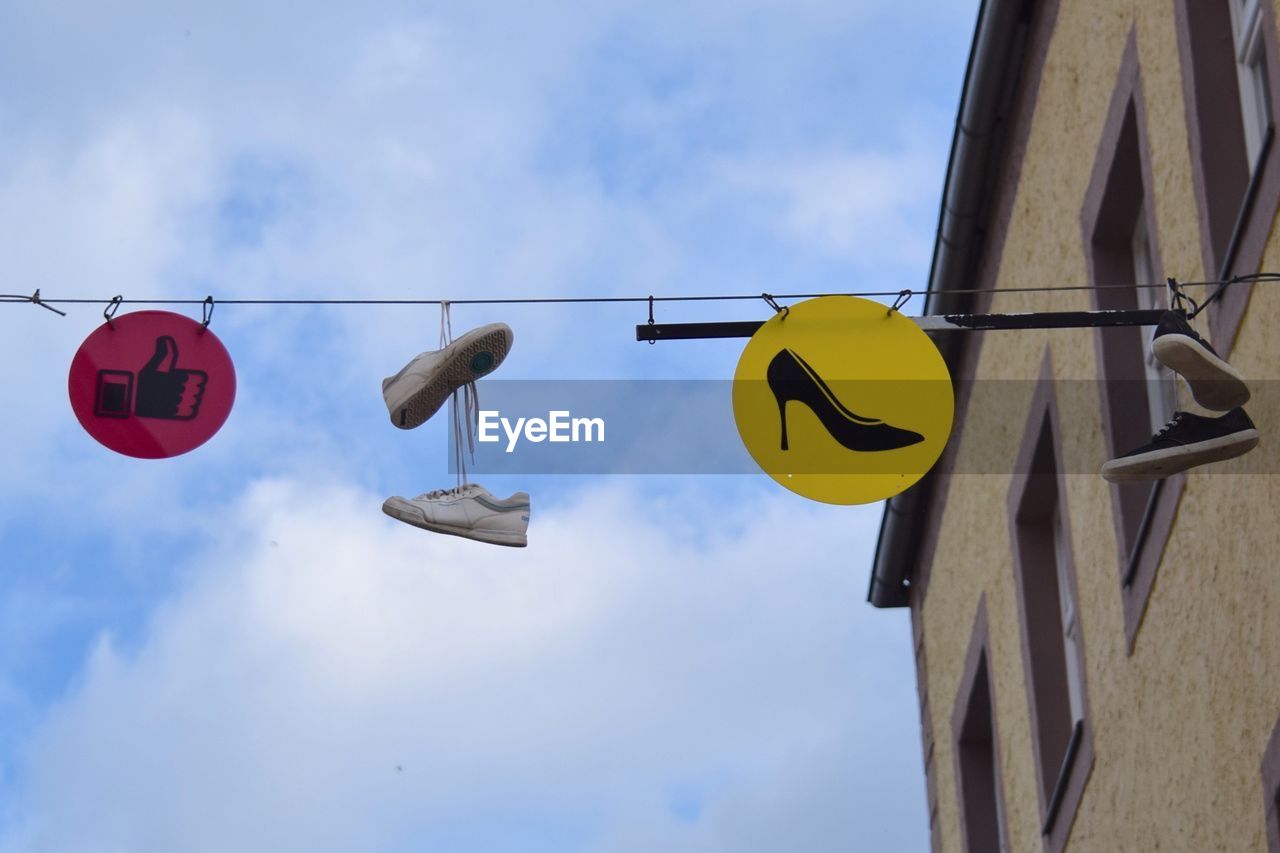 Low angle view of shoes hanging on cable against cloudy sky