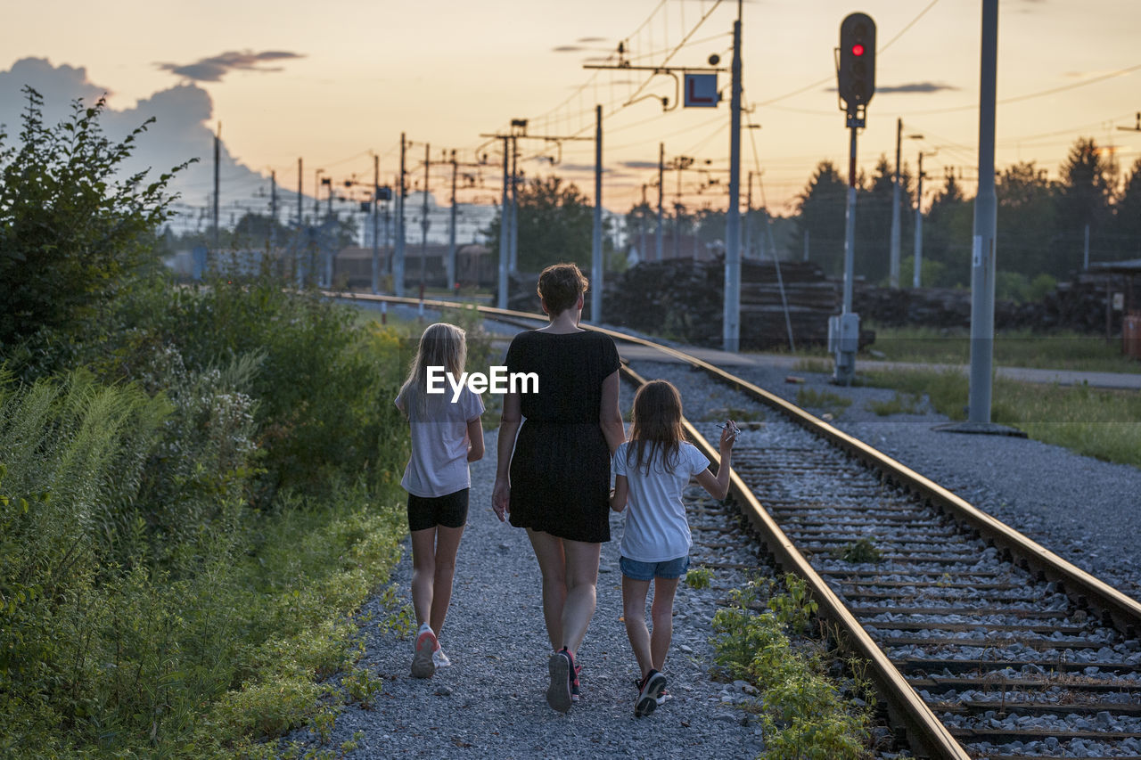 Rear view of family by railroad tracks during sunset