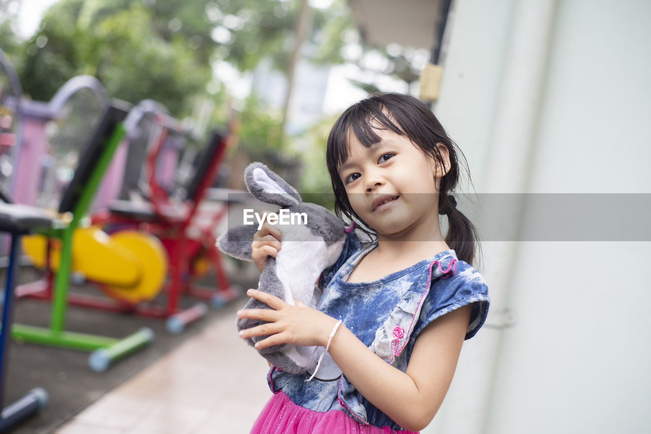 Portrait of cute girl holding stuffed toy while standing outdoors