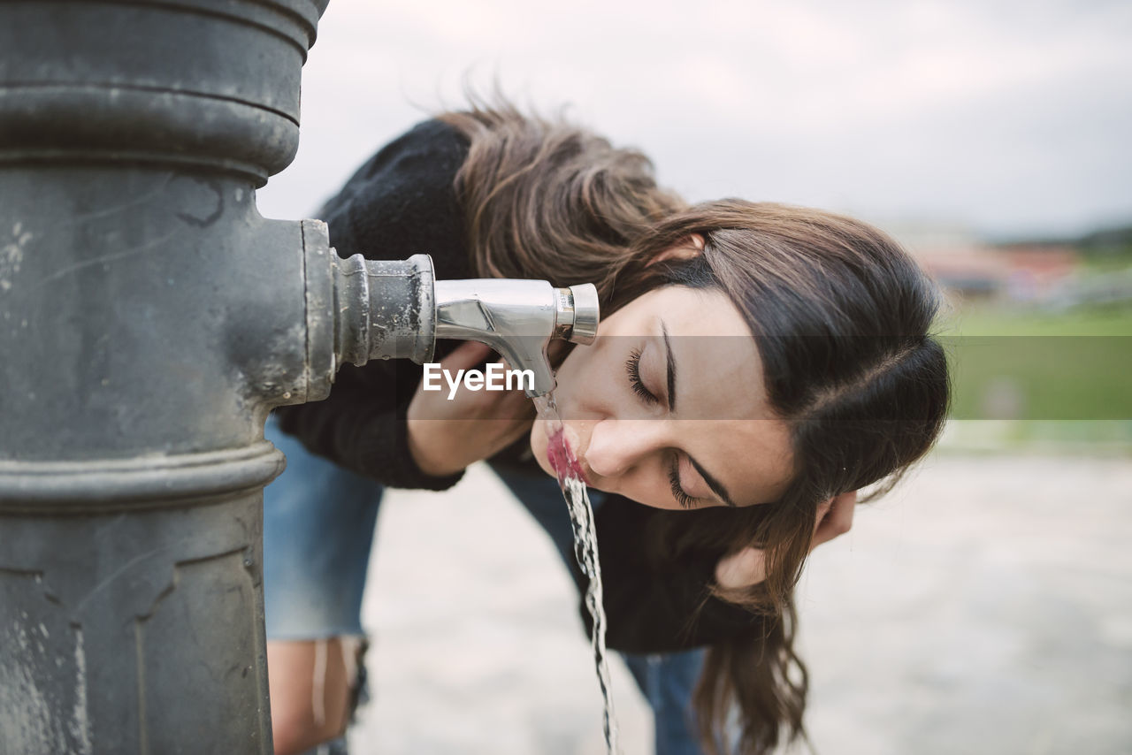 Young woman drinking water from a well