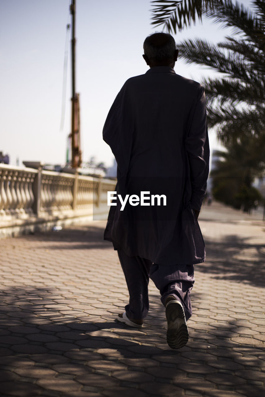 Rear view of man walking on footpath against clear sky