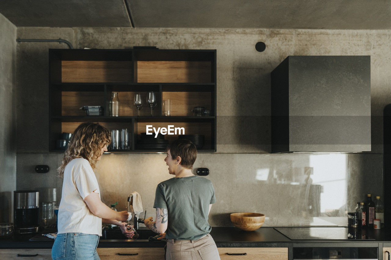 Happy lesbian couple washing dishes while standing in kitchen at home