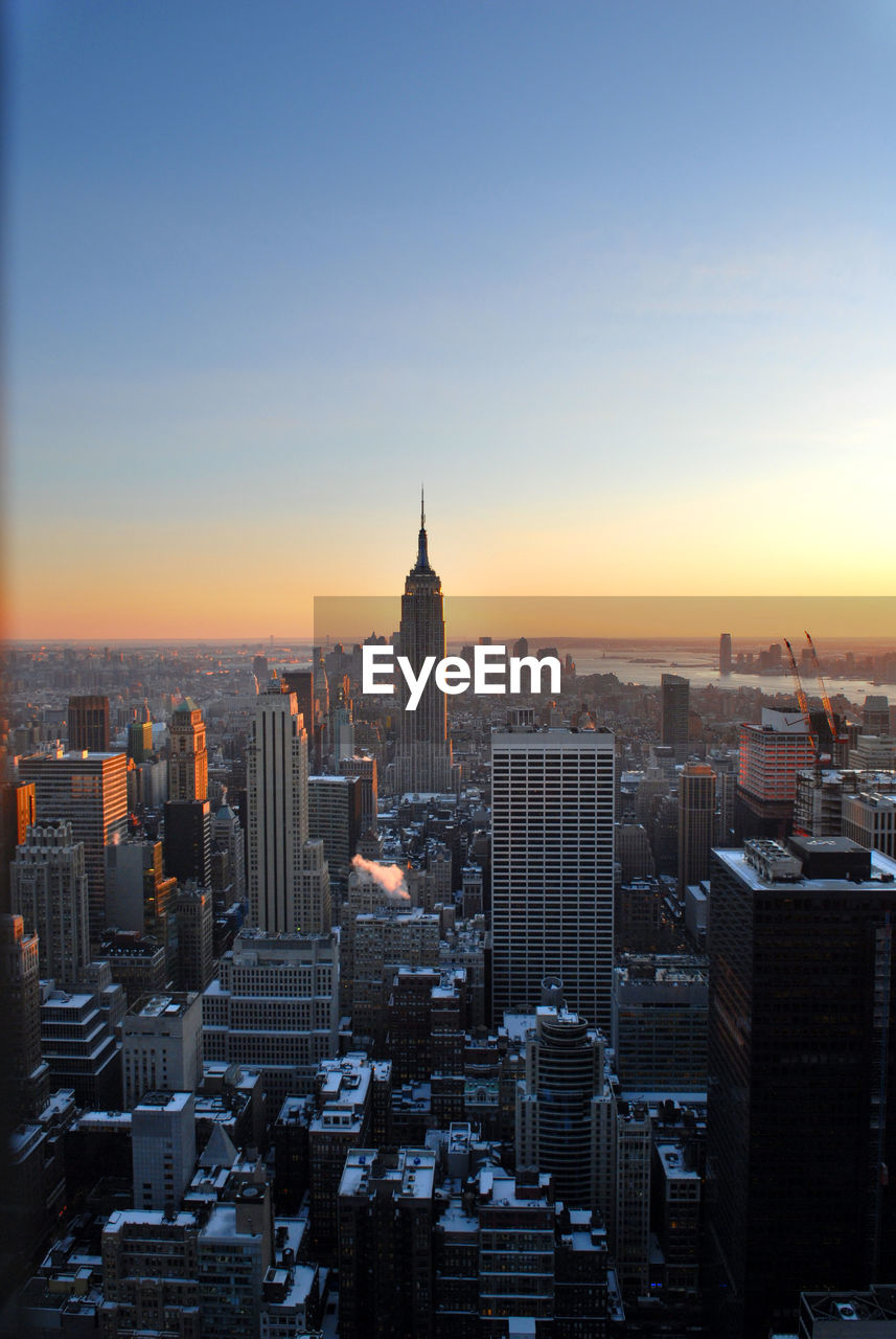 Mid distance of empire state building amidst cityscape against sky during sunset
