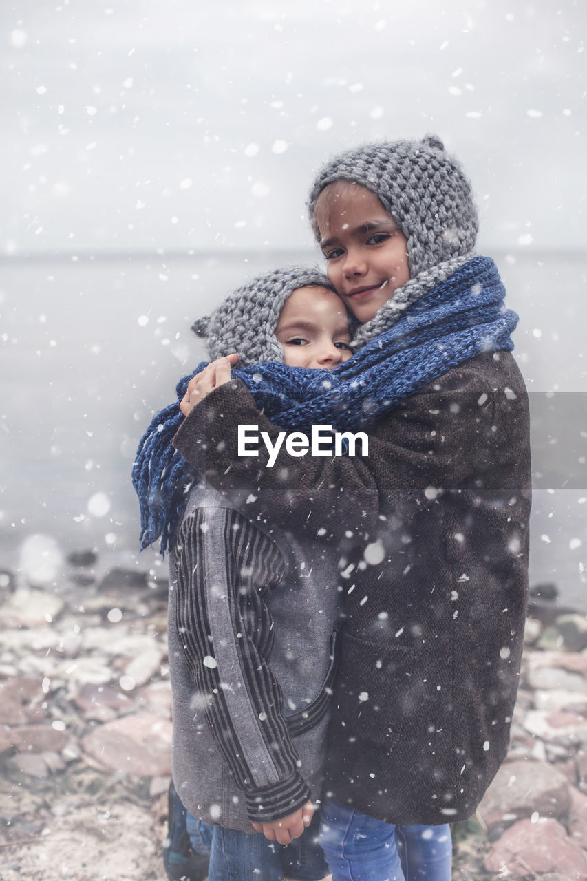 Girl in knitted grey hat hugging her frozen smaller brother