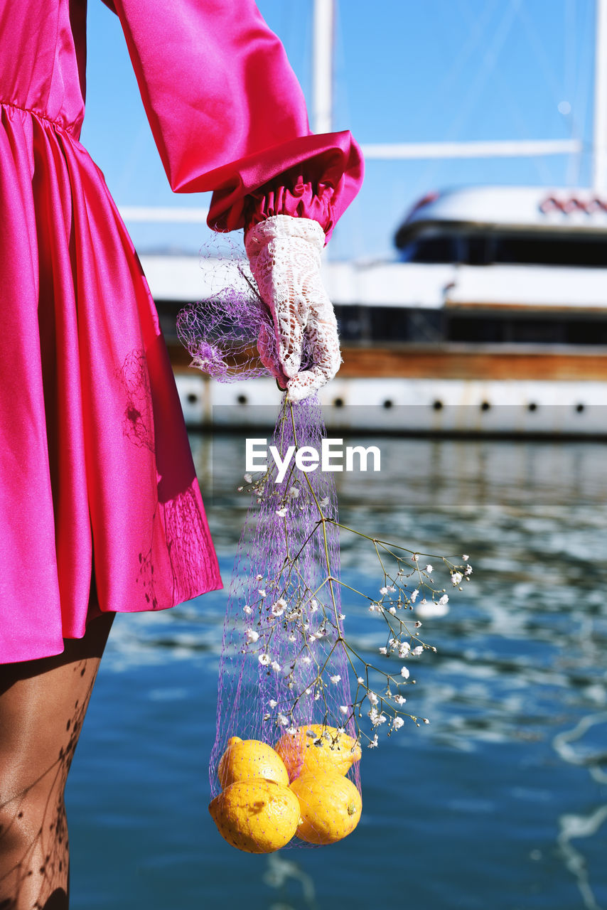 Midsection of woman holding lemon in net by water