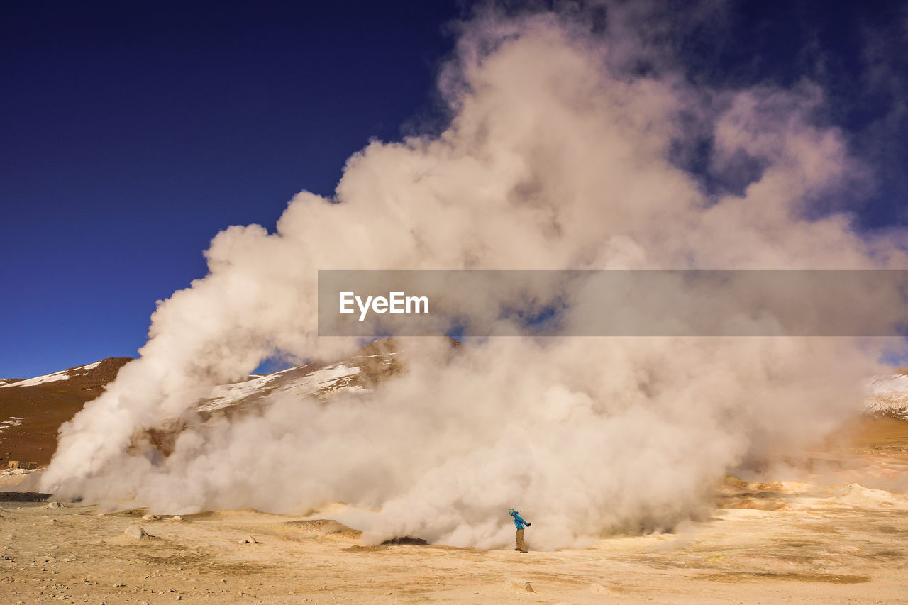 Man standing by geyser smoke against sky