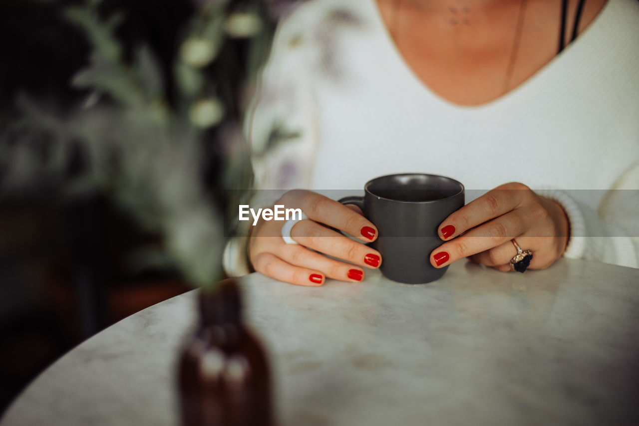 Midsection of woman holding cup of coffee while sitting at table