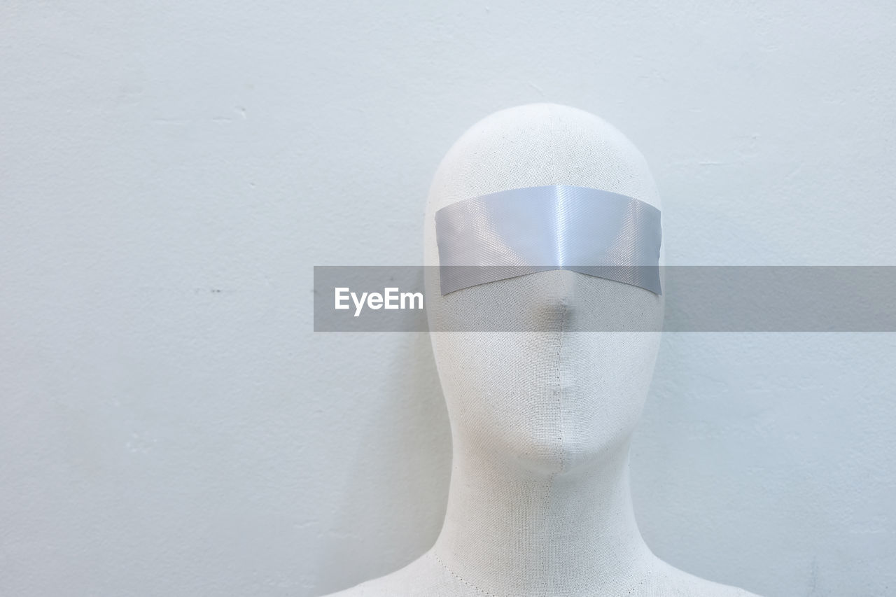 Close-up of mannequin with blind fold against wall