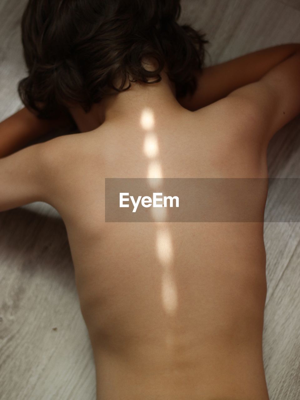 Rear view of shirtless boy lying on floor at home