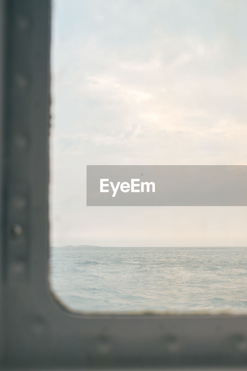 View through a ship window on the light blue sea against a light blue cloudy sky