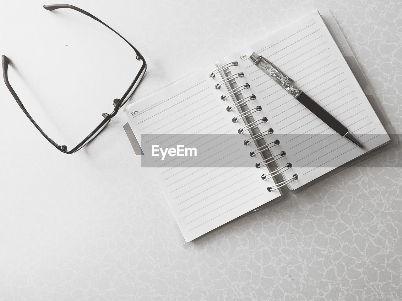 Directly above shot of pen and diary with eyeglasses on white table