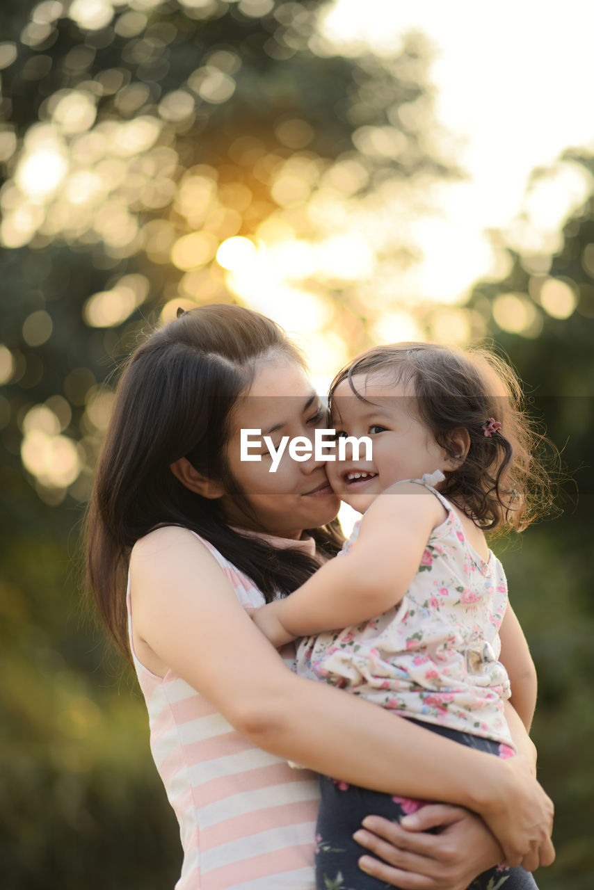 Happy mother with daughter standing against trees