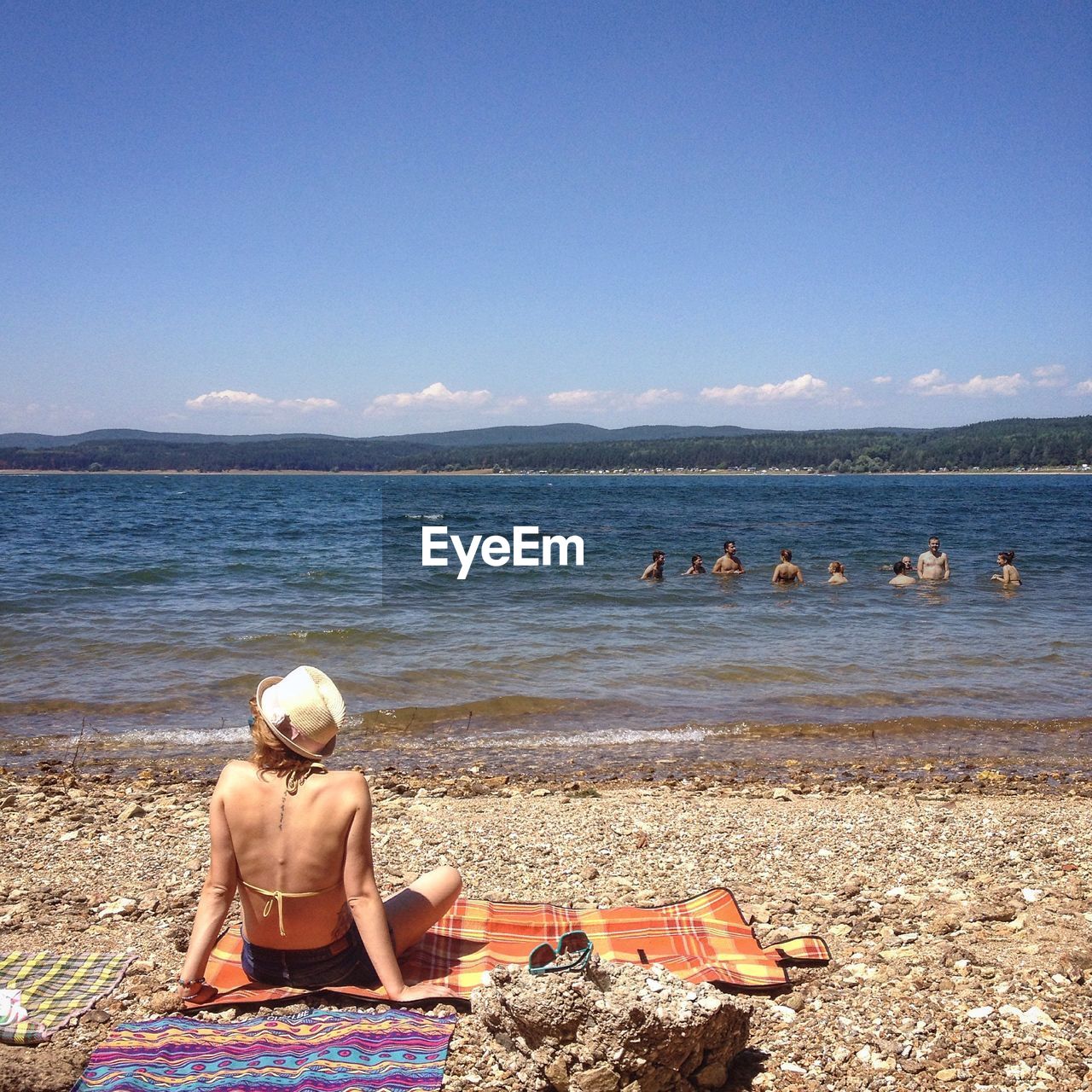 REAR VIEW OF WOMAN SITTING ON SHORE AT BEACH
