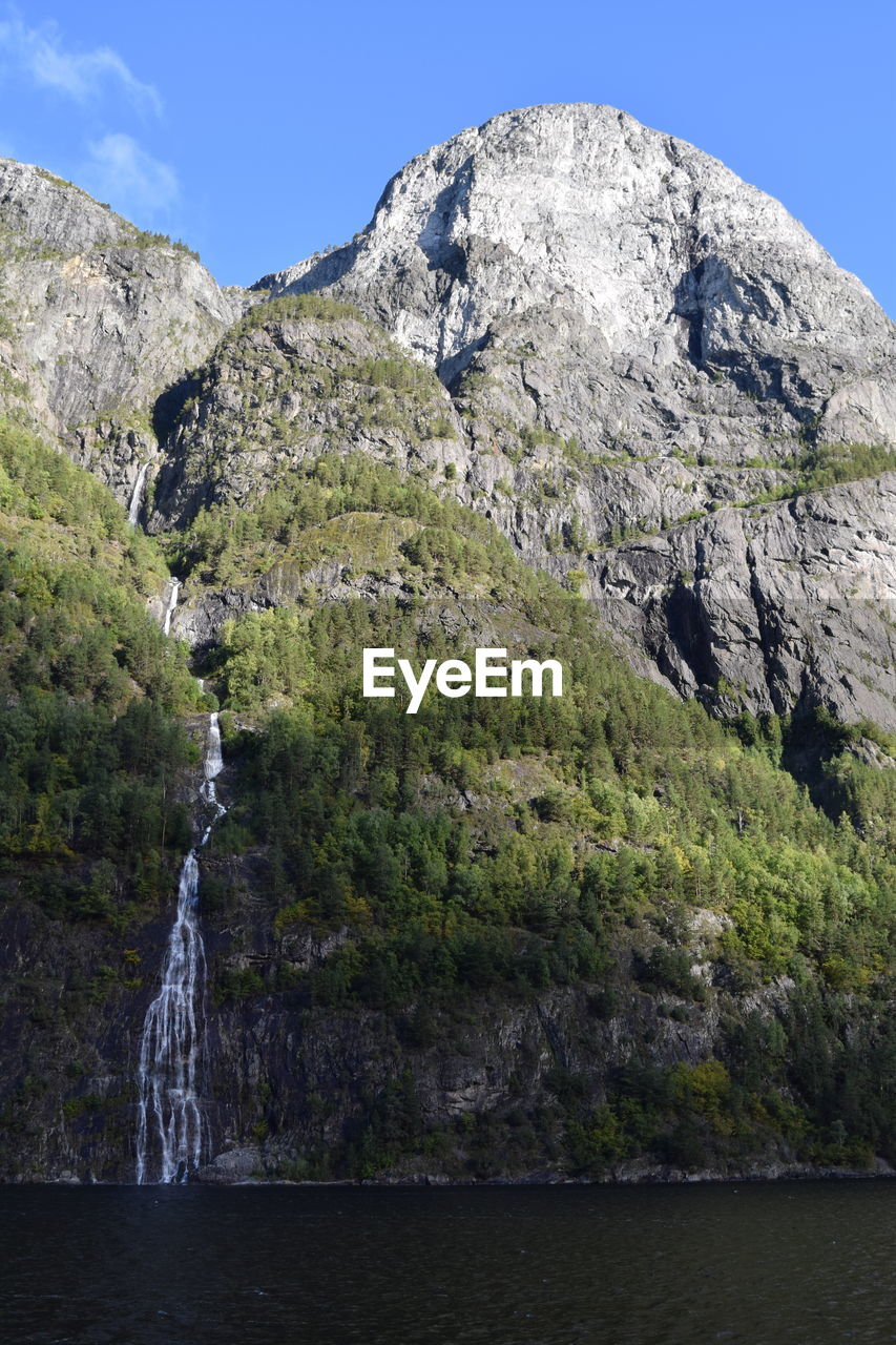 SCENIC VIEW OF WATERFALL BY MOUNTAINS AGAINST SKY