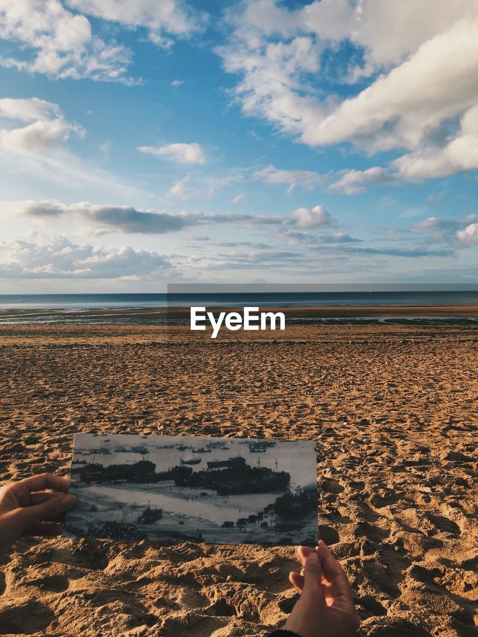 Cropped hands holding photograph against beach