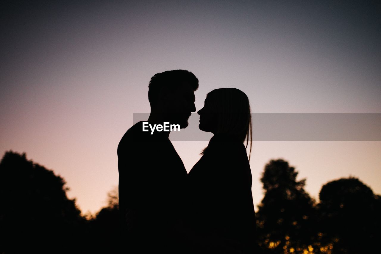 Side view of silhouette couple standing against sky during sunset