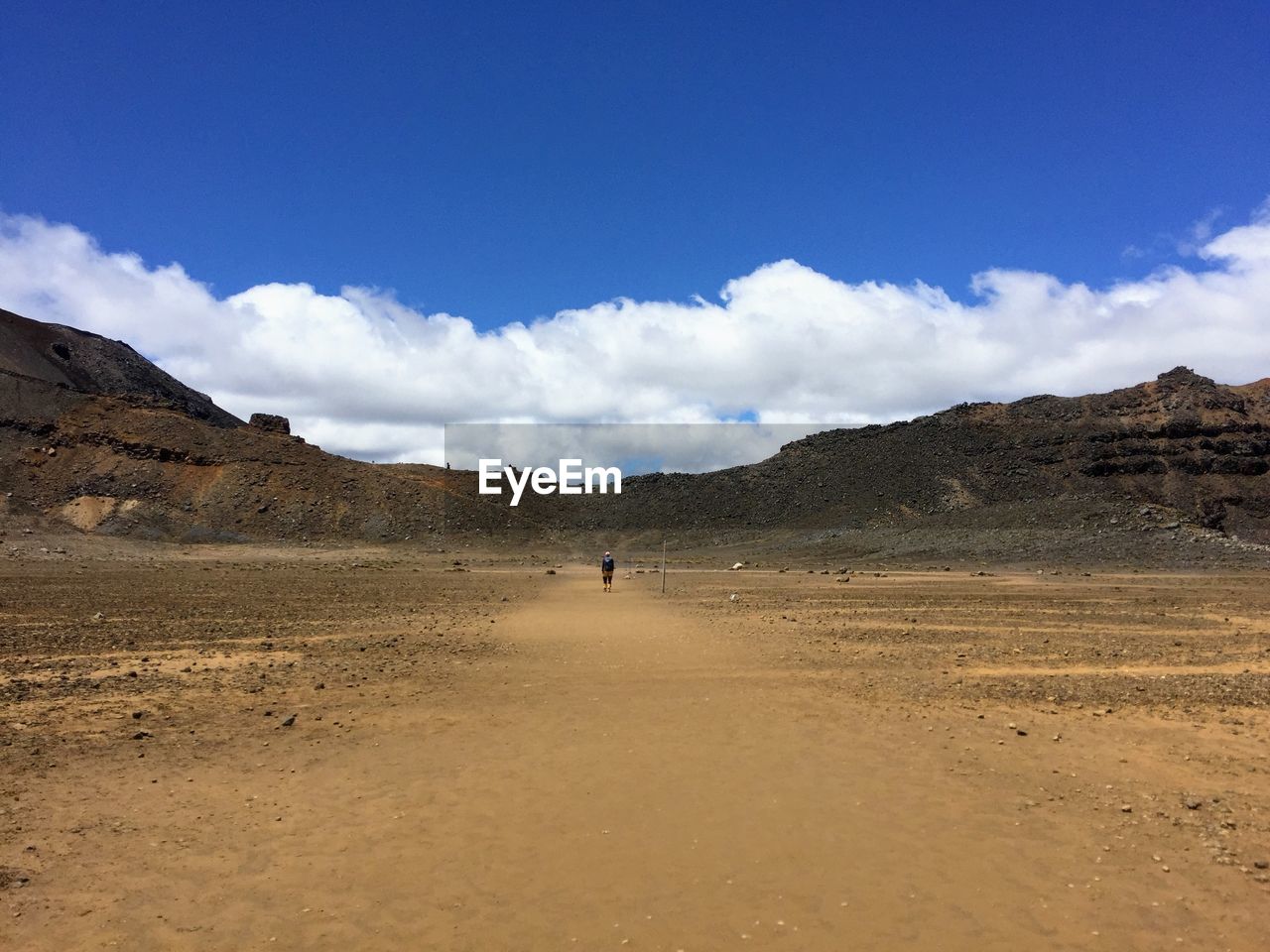 Mid distance view of woman walking at desert against blue sky