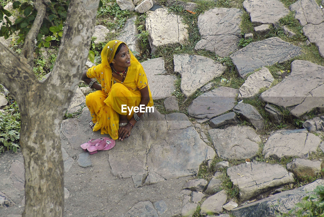 High angle view of smiling woman in yellow sari sitting on rock