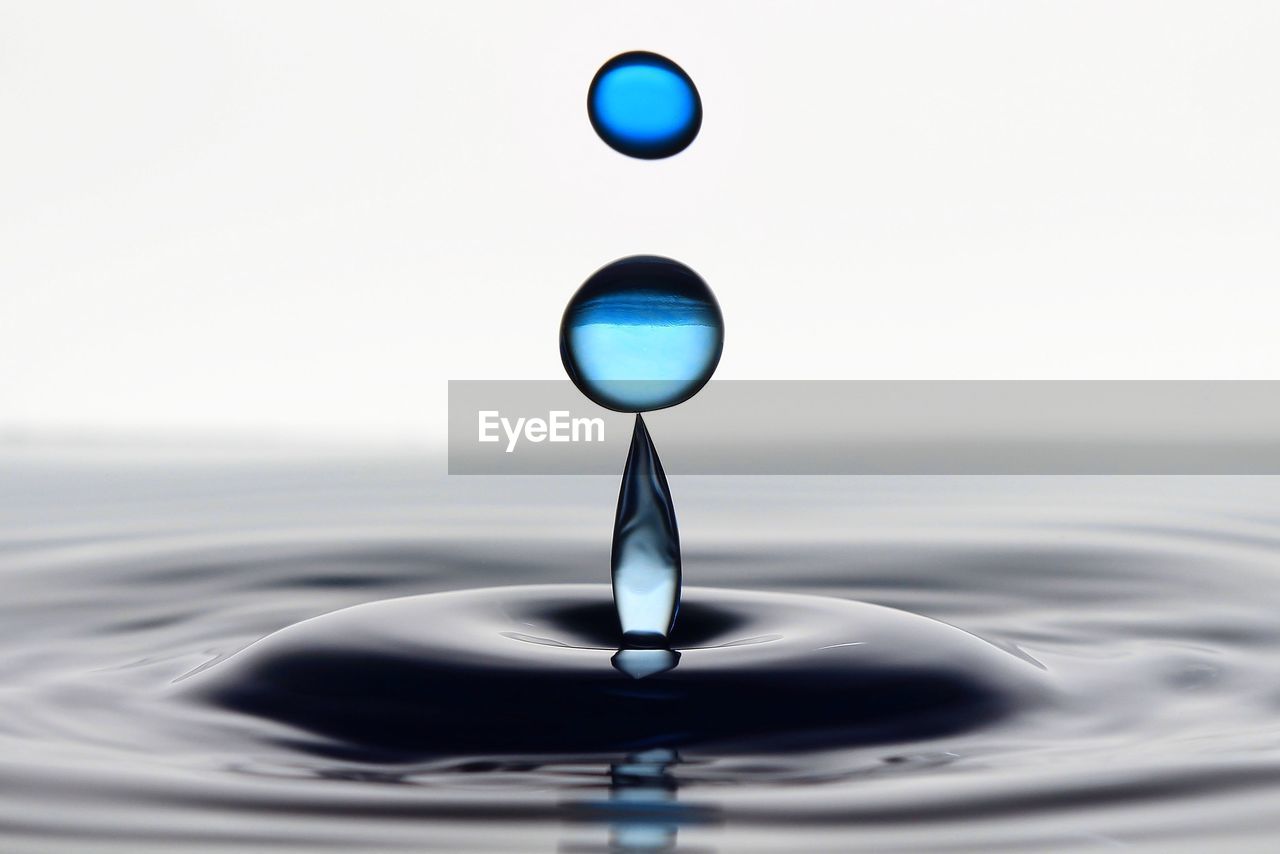 Close-up of droplets falling on water against white background