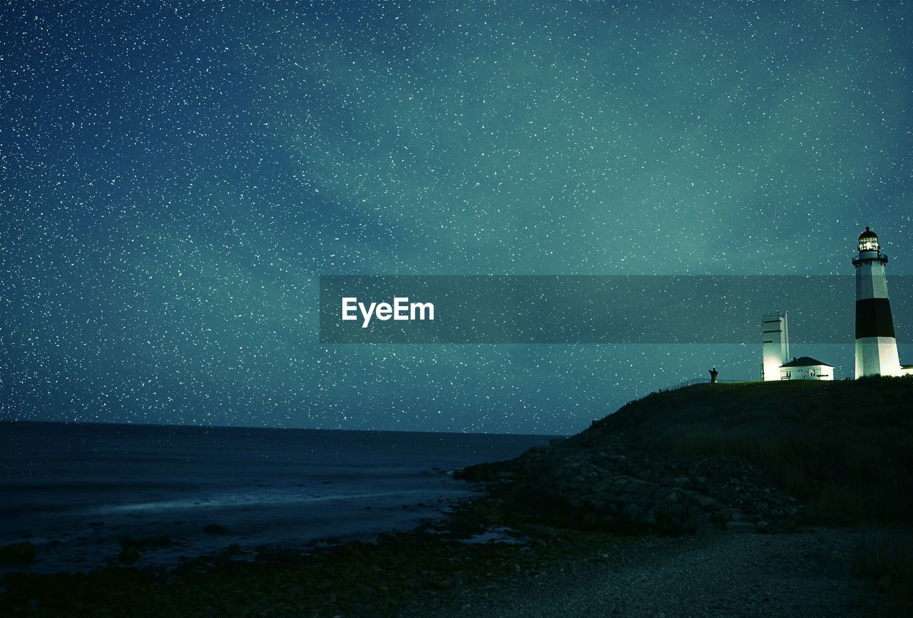 Illuminated montauk point light on shore against star field at night