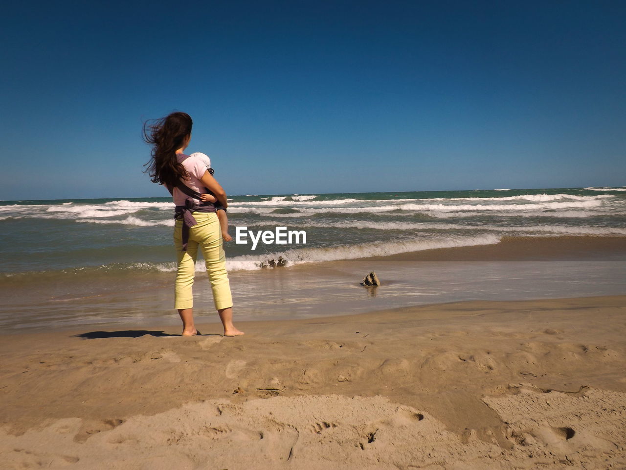 Rear view of mid adult woman with son standing at beach against clear sky