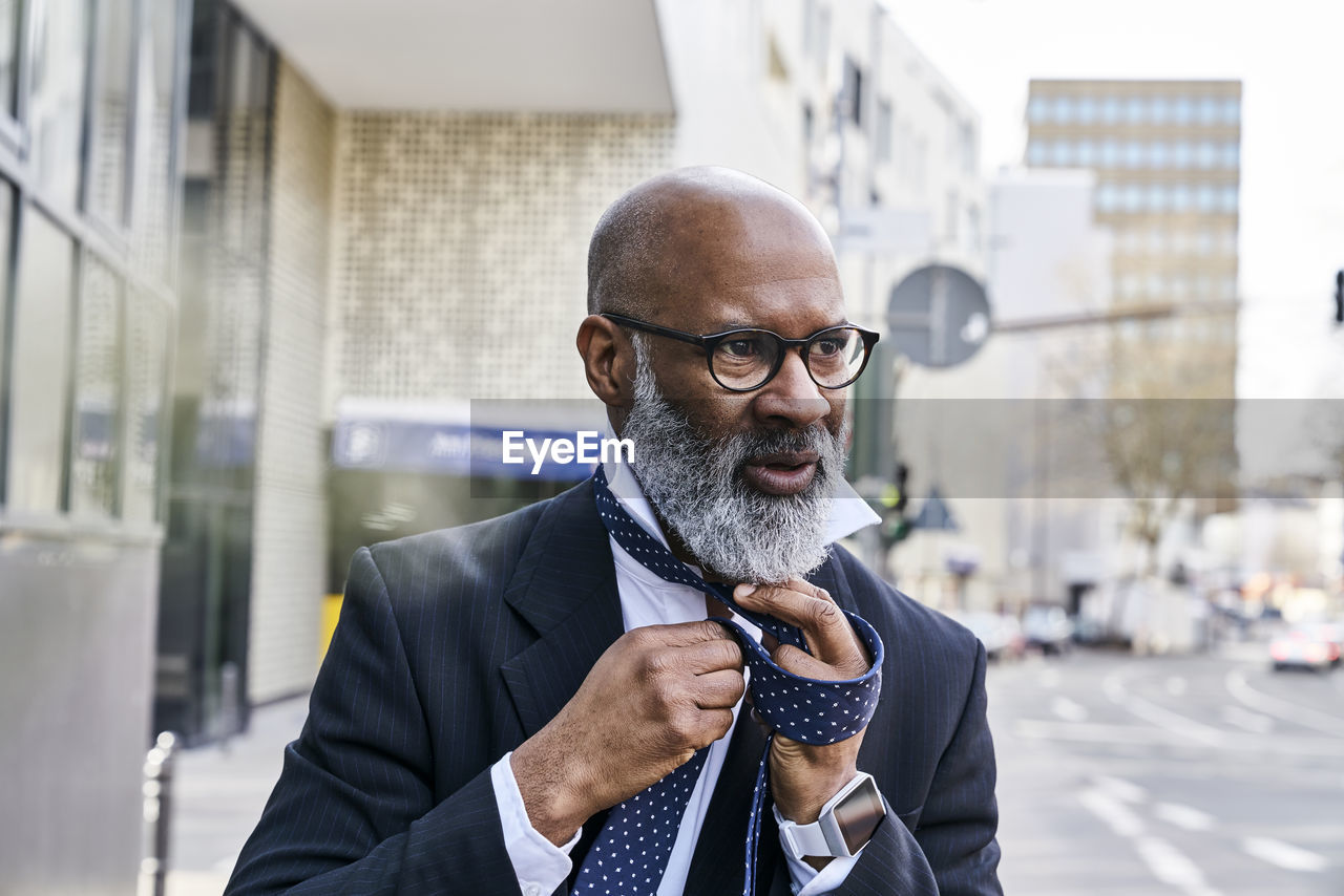 Mature businessman tying tie in the street