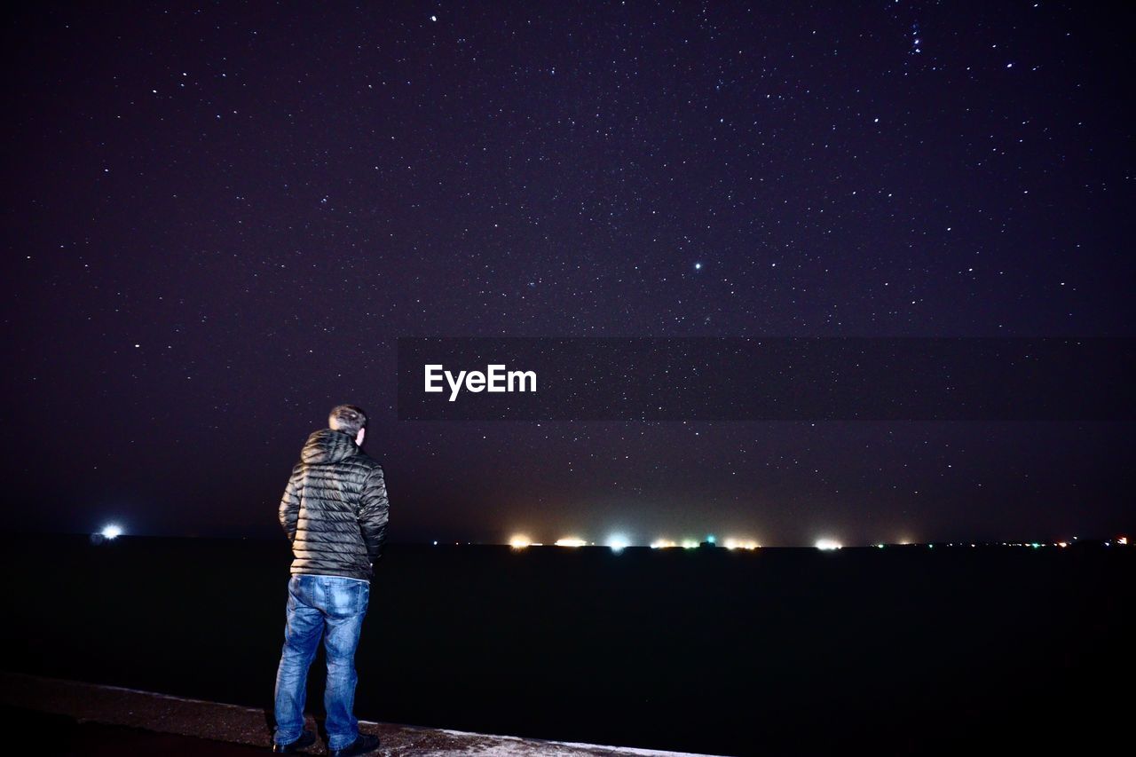 REAR VIEW OF WOMAN STANDING AGAINST ILLUMINATED STAR FIELD AGAINST SKY