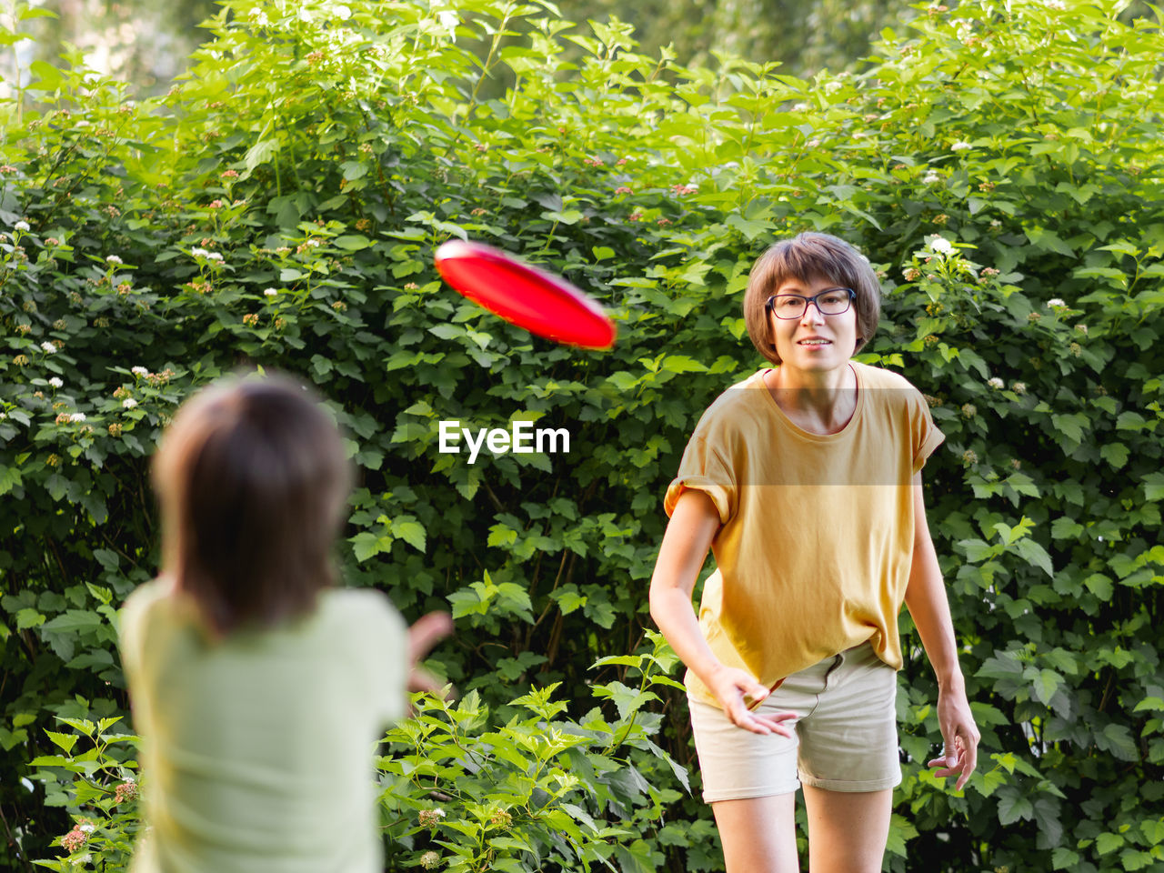 Mother and son play frisbee on grass lawn. summer vibes. family life. sports game at backyard.