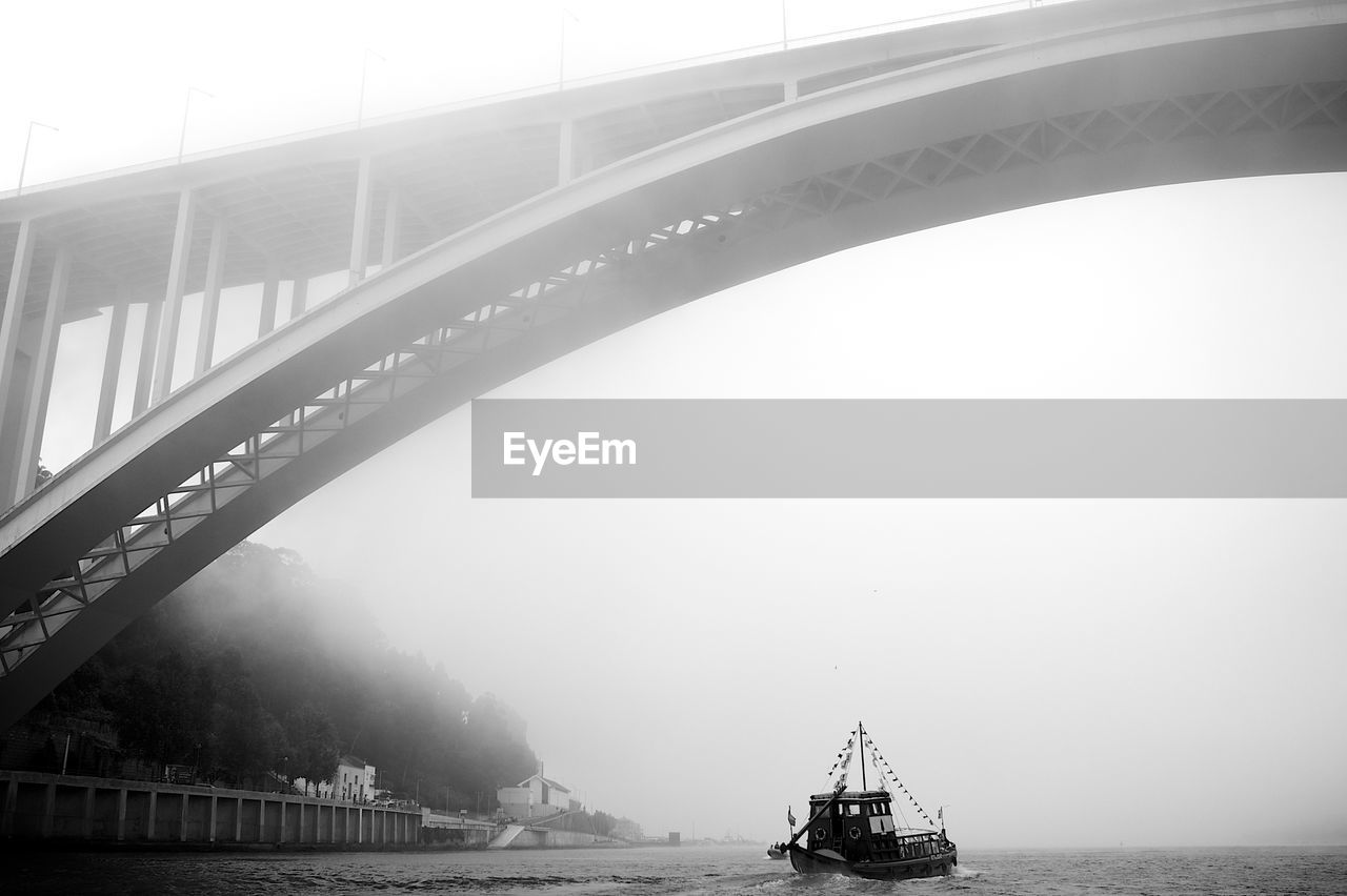 Arrabida bridge below trawler sailing on douro river in foggy weather