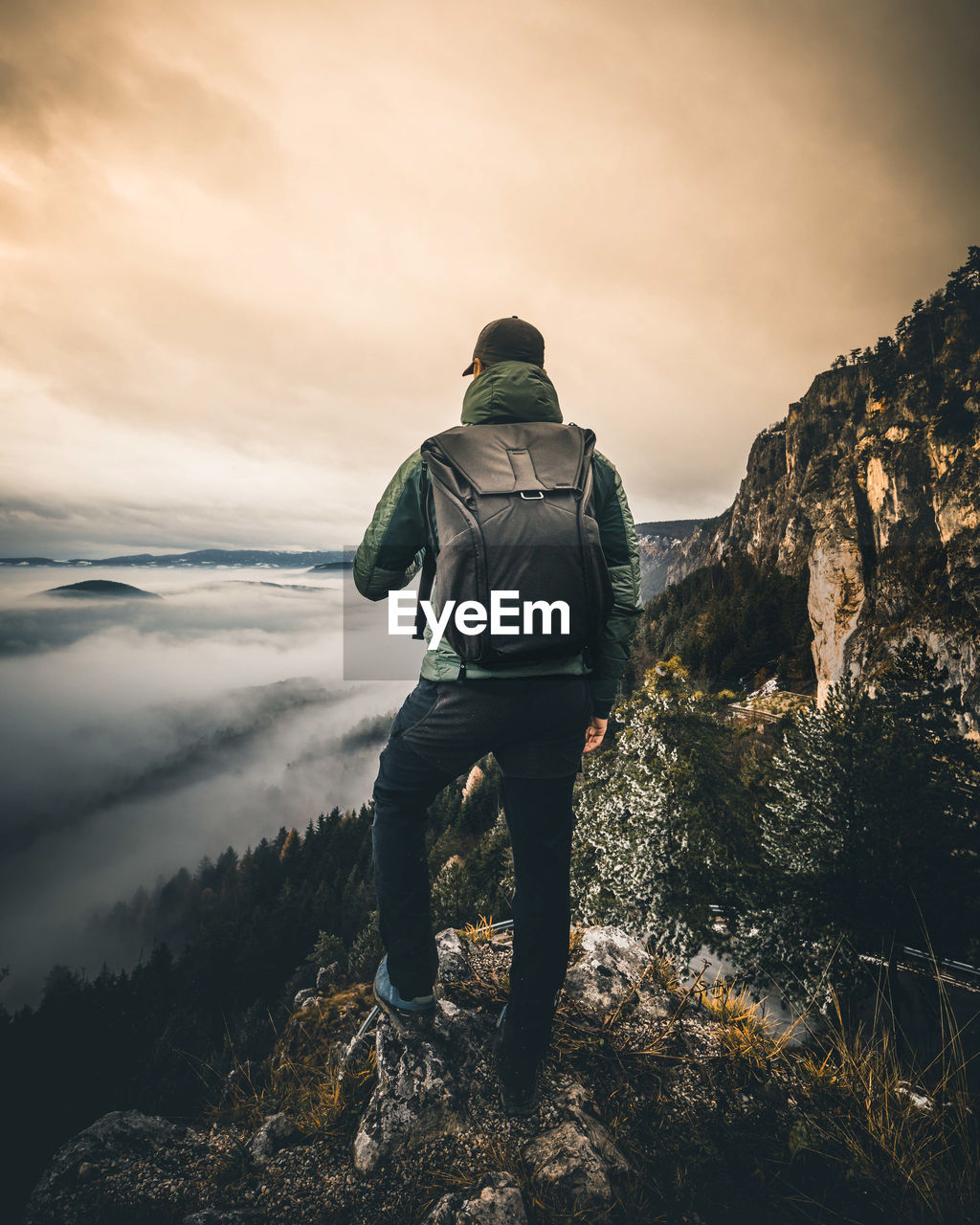REAR VIEW OF MAN STANDING ON ROCKS AGAINST SKY