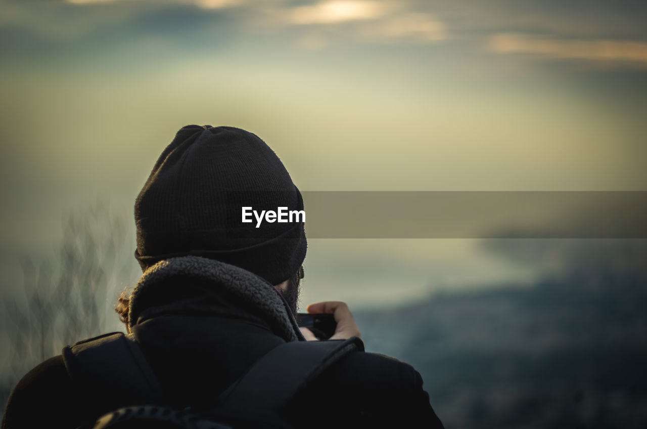 Rear view of man wearing warm clothing against sky at sunset