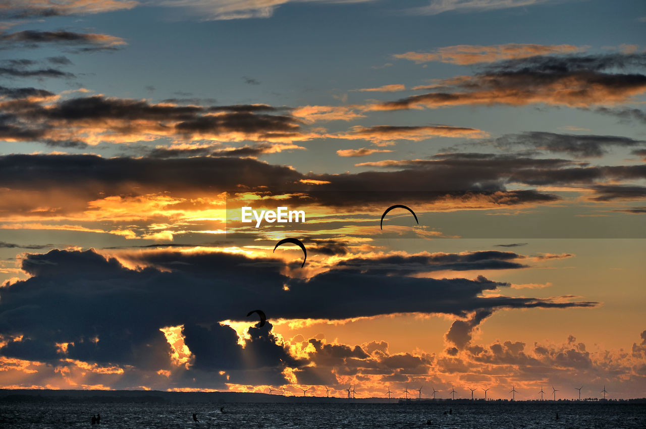 SILHOUETTE BIRD FLYING OVER SEA AGAINST SKY DURING SUNSET