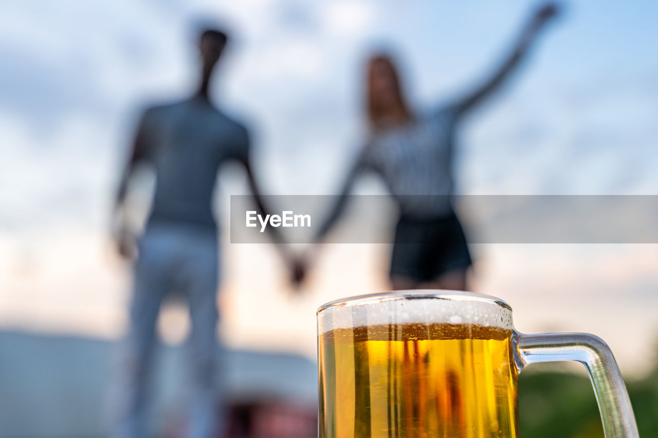 beer, refreshment, drink, food and drink, alcohol, sky, adult, focus on foreground, drinking glass, glass, beer glass, nature, women, leisure activity, two people, relaxation, togetherness, household equipment, men, cloud, summer, outdoors, friendship, day, young adult, standing, enjoyment, water, emotion, casual clothing, vacation