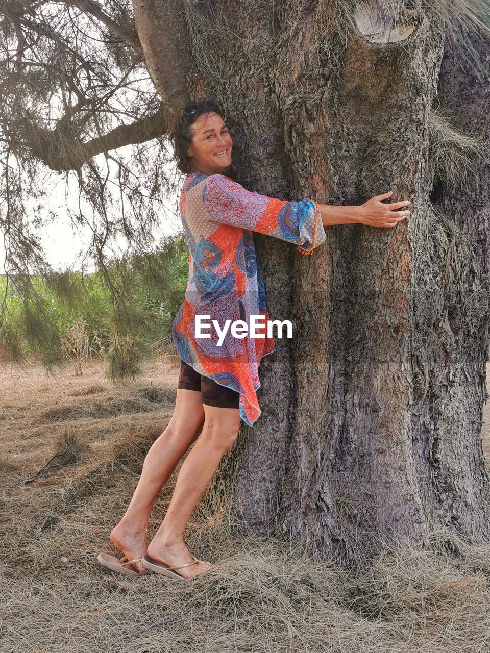 full length, one person, leisure activity, tree, land, casual clothing, plant, nature, lifestyles, day, childhood, women, child, smiling, adventure, happiness, outdoors, front view, female, carefree, enjoyment, person, rock climbing, clothing, tree trunk, standing, sports, trunk, adult, emotion, barefoot, young adult, fun, holiday, motion, portrait