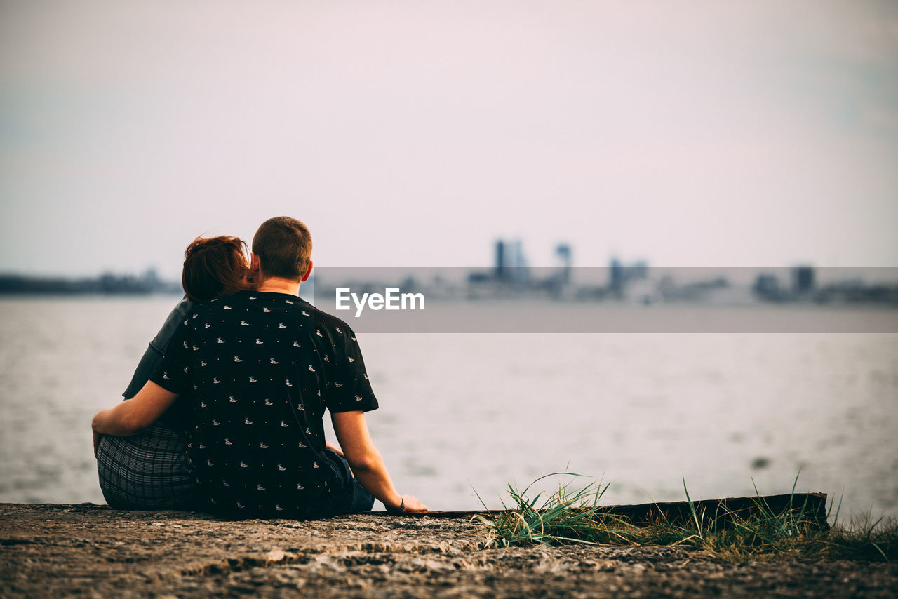 REAR VIEW OF MAN AND WOMAN LOOKING AT SEA