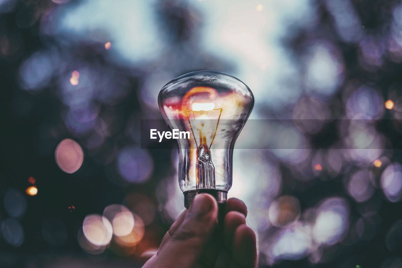 Cropped image of hand holding illuminated light bulb during sunset