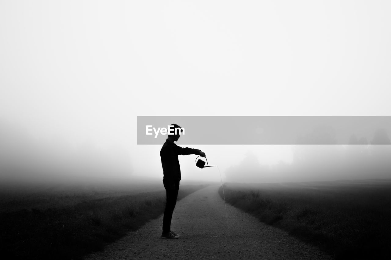 SILHOUETTE MAN STANDING ON MOUNTAIN DURING FOGGY WEATHER