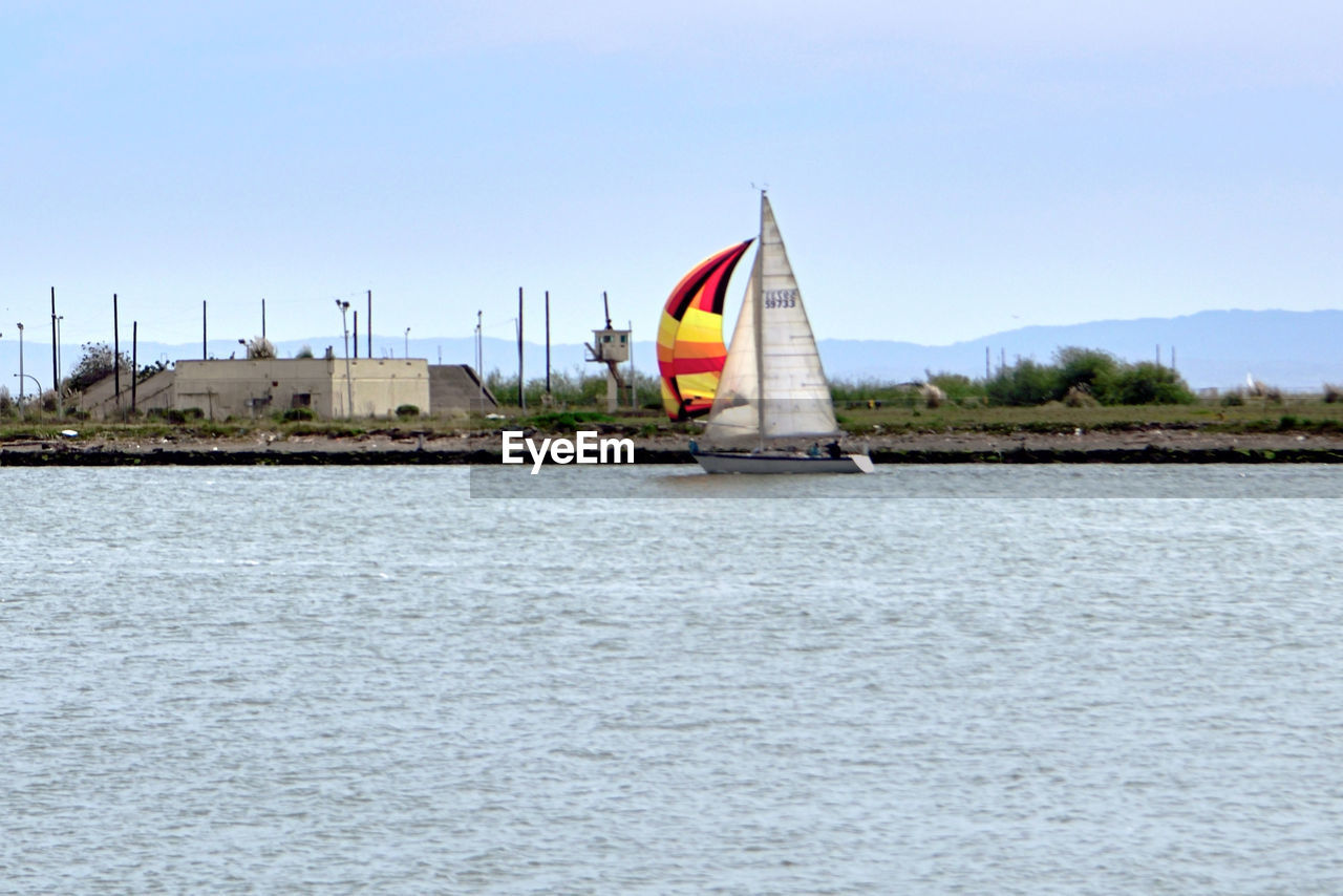 SAILBOAT SAILING ON RIVER AGAINST SKY