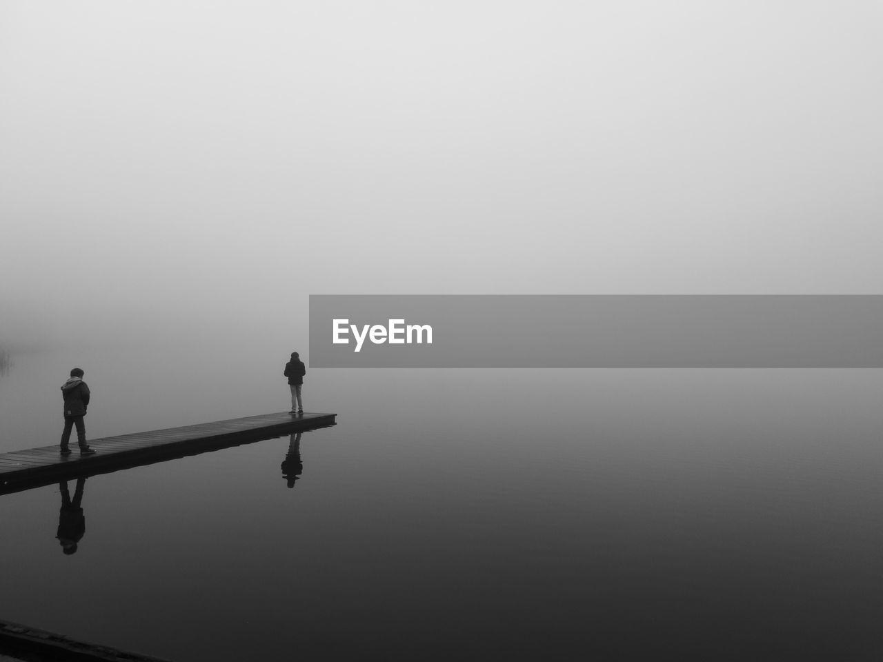 People standing on pier over lake during foggy weather