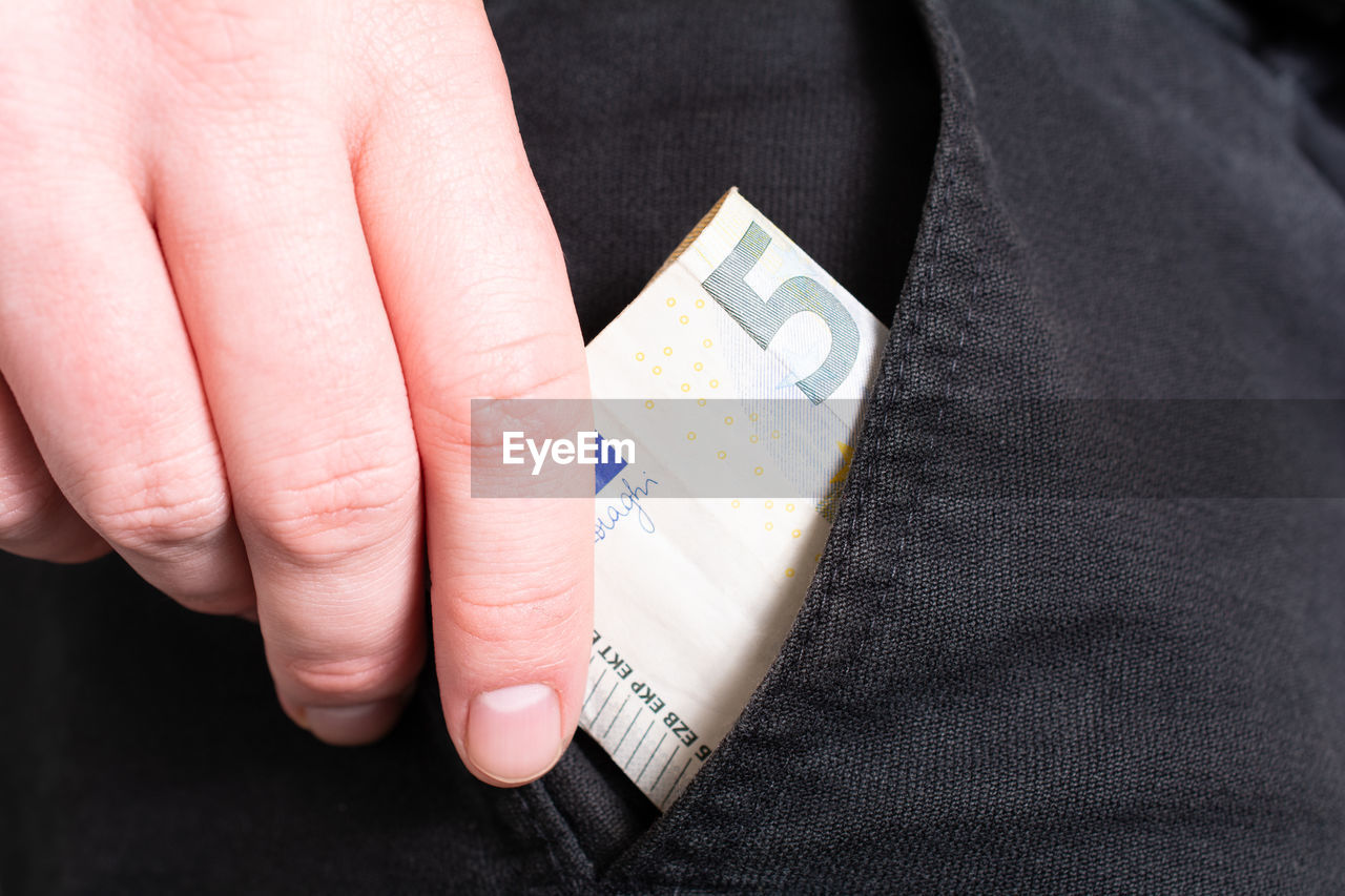 Close up of person putting paper currency in pocket