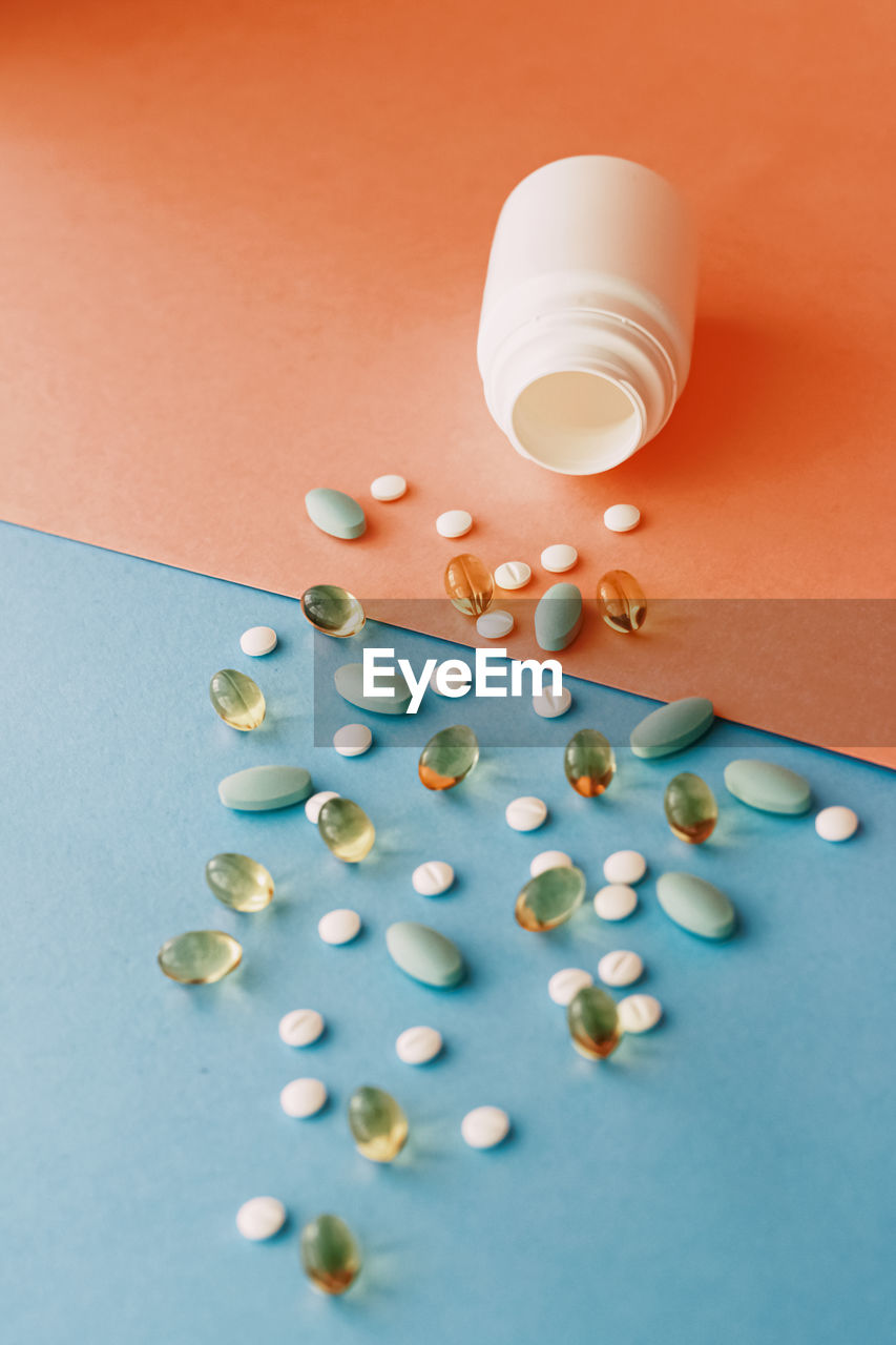 high angle view of pills spilling from bottle on blue background