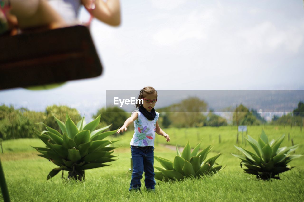 Portrait of girl standing on grassy field against cloudy sky