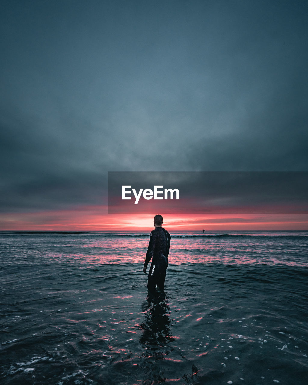 MAN STANDING AT SEA AGAINST SKY DURING SUNSET