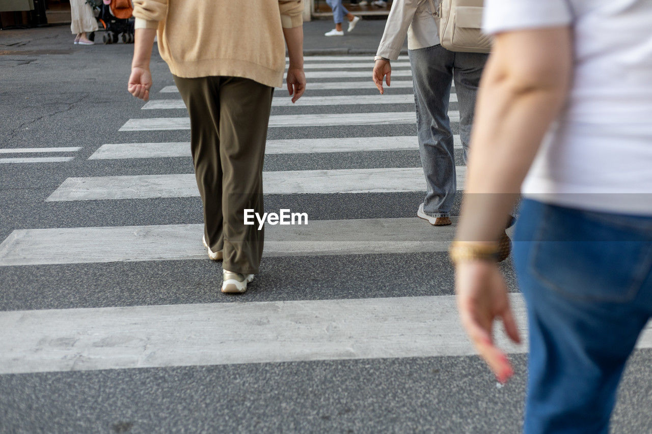 crosswalk, crossing, city, zebra crossing, road marking, walking, group of people, street, road, transportation, architecture, motion, symbol, city life, adult, low section, marking, pedestrian crossing, city street, men, women, blurred motion, on the move, sign, human leg, day, spring, commuter, infrastructure, outdoors, limb, human limb, clothing, casual clothing, lifestyles, crowd, trousers, jeans, rear view, footwear