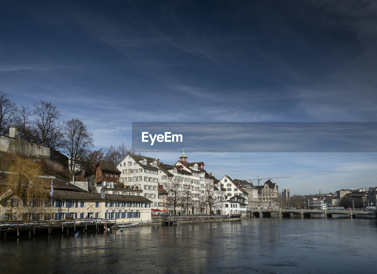 Buildings by river against sky in city