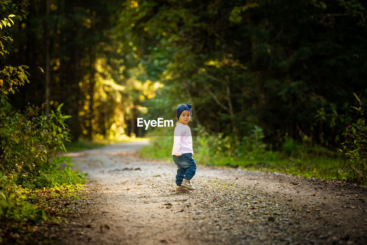 Full length of baby girl standing on dirt road amidst forest