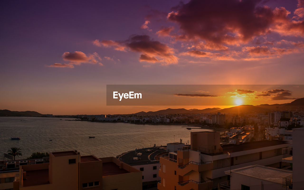 Town by sea against sky during sunset